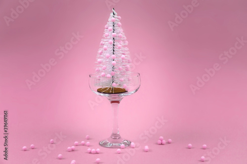 Christmas tree with pink decoration in glass of champagne on pink background. Christmas composition. New year minimalistic composition. Holiday concept.