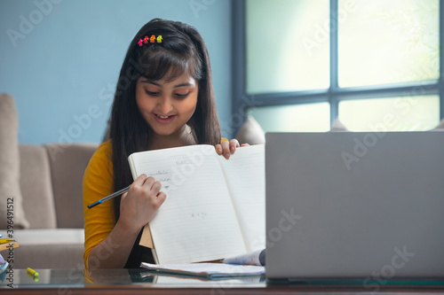 Young girl showing the spellings of the words her teacher dictated in front of the laptop during online class 