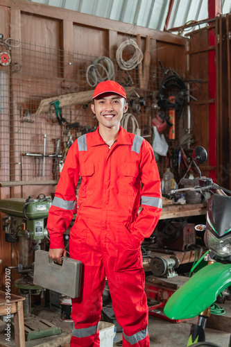 mechanic wearing the wearpack stands carrying the toolbox in the workshop background photo