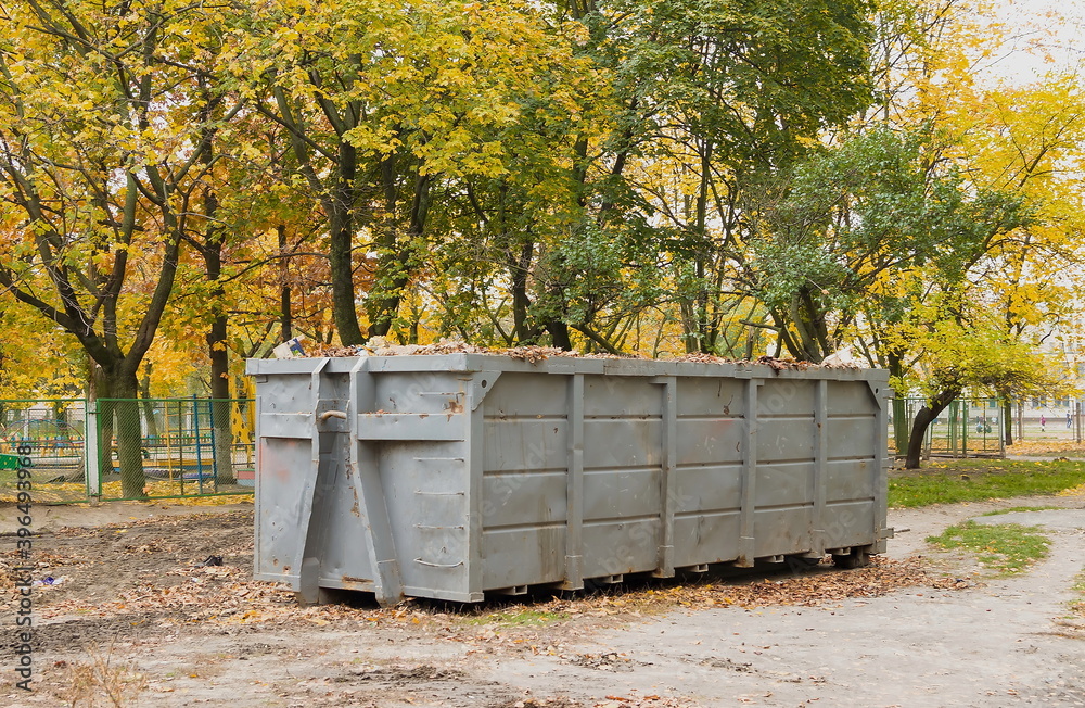 Container for collecting cut grass and fallen leaves in autumn. Large metal container for household waste. Cleaning of fallen leaves and grass. Putting order in parks and squares
