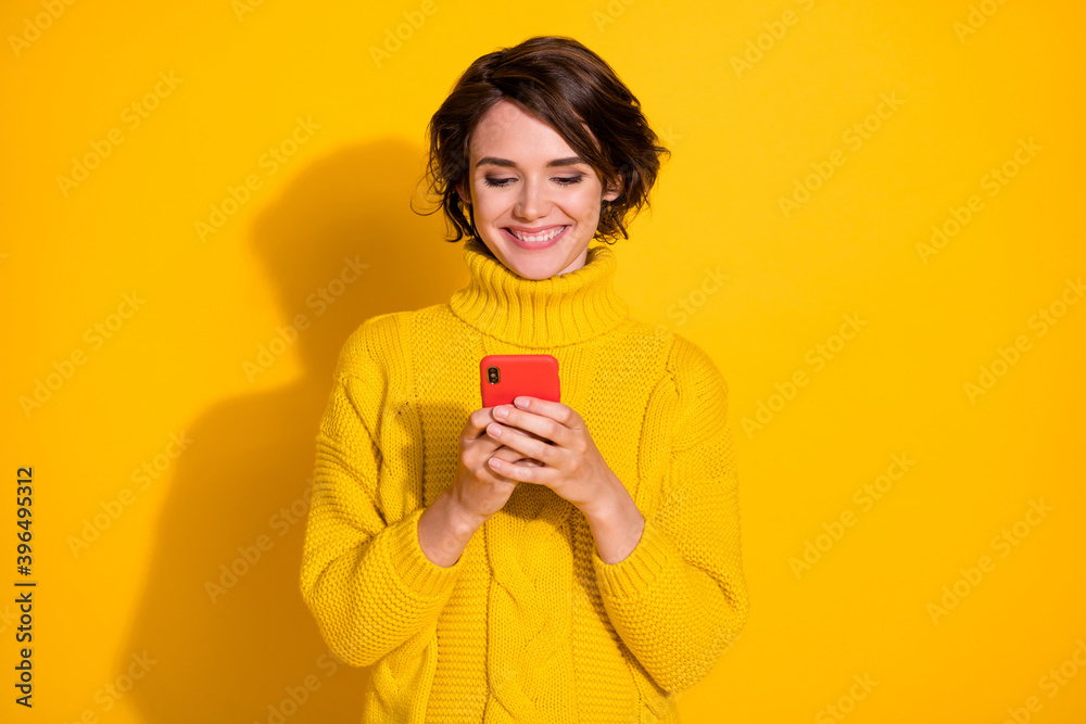 Photo portrait of smiling female brunette browsing internet wearing knitted sweater isolated on vivid yellow color background Photo portrait of smiling female brunette browsing internet wearing knitted sweater isolated on vivid yellow color background