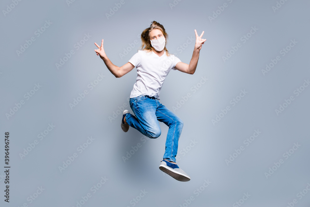 Photo of funky long blonde hair guy dressed casual clothes mask jumping up demonstrating v-sign isolated grey color background Photo of funky long blonde hair guy dressed casual clothes mask jumping up demonstrating v-sign isolated grey color background