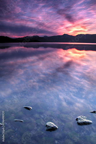 ドラマチックな空を湖面に反射するカルデラ湖。湖岸からの夕暮れの風景。