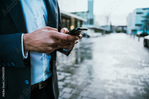 Close up of mixed race businessman texting on mobile device standing outside office block