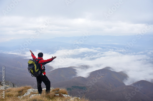 Man on cliff rise hands and enjoy looking on a clouds under mountain. Man hiking in the mountains in fog. Dry Mountain, Serbia in autumn