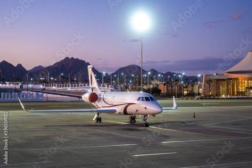 Business Airplane Parking Outside The Terminal In  Airport. Private Jet Airliner, Luxury Corporate Aircraft, Airport Lights, Sunset Over The Mountains.