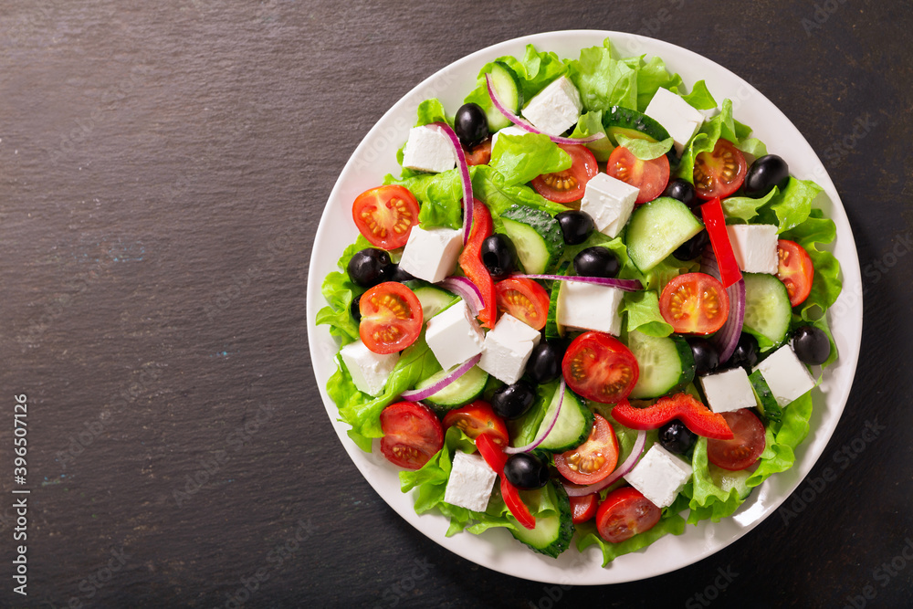 Plate of fresh salad with vegetables, feta cheese and olives. Greek salad. Top view