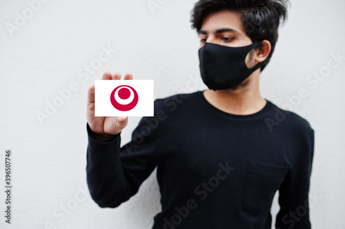 Japanese man wear all black with face mask hold Okinawa flag in hand isolated on white background. Prefectures of Japan сoronavirus concept. photo