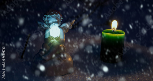 Angel (figurine) and a green candle on the snow. Christmas decoration. Greetings card, cover book