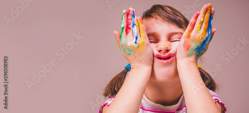 Funny portrait of happy beautiful young child girl makes faces with children's makeup and painting colorful hands. Free space for text or design.