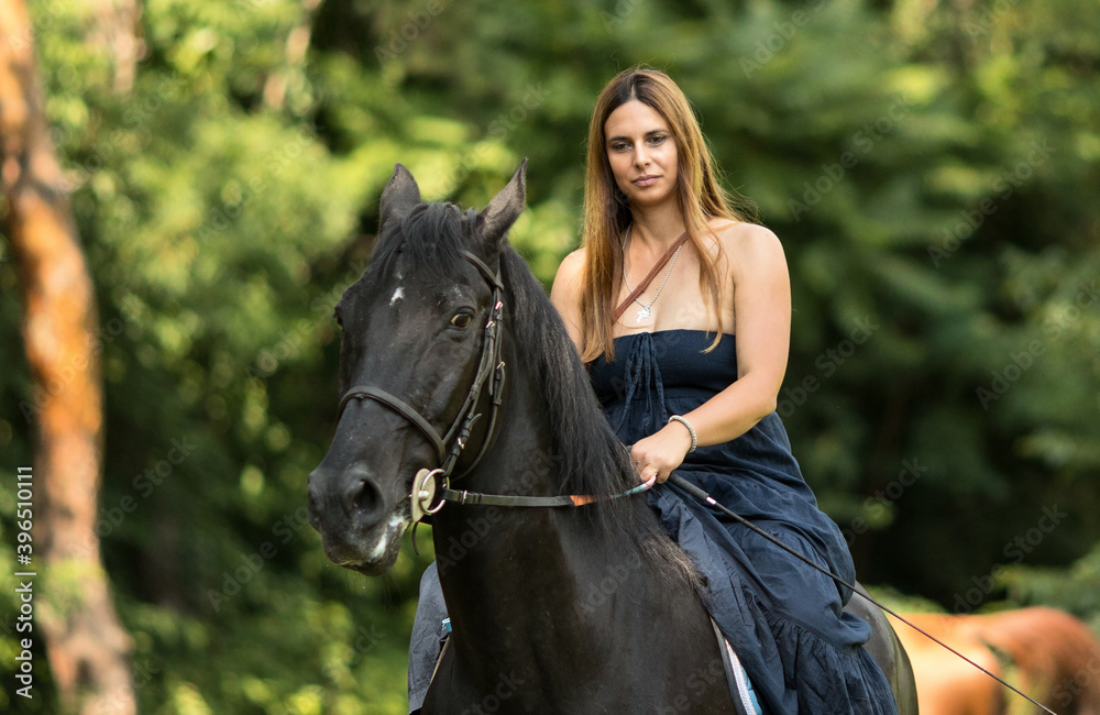 Girl with a long copper hair and long flowy shoulderless dress, ride a black horse with trees in the background. Girl with a long copper hair and long flowy shoulderless dress, ride a black horse with trees in the background.