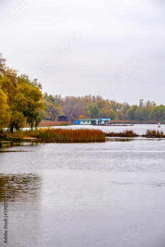 View of  a little house close to the Dnieper river in Kiev, Ukraine, at the beginning of autumn, under a clean gray sky. Plants and reeds in the forground.