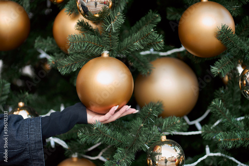 Close up view of woman's hand holding a golden ball on the christmas tree.