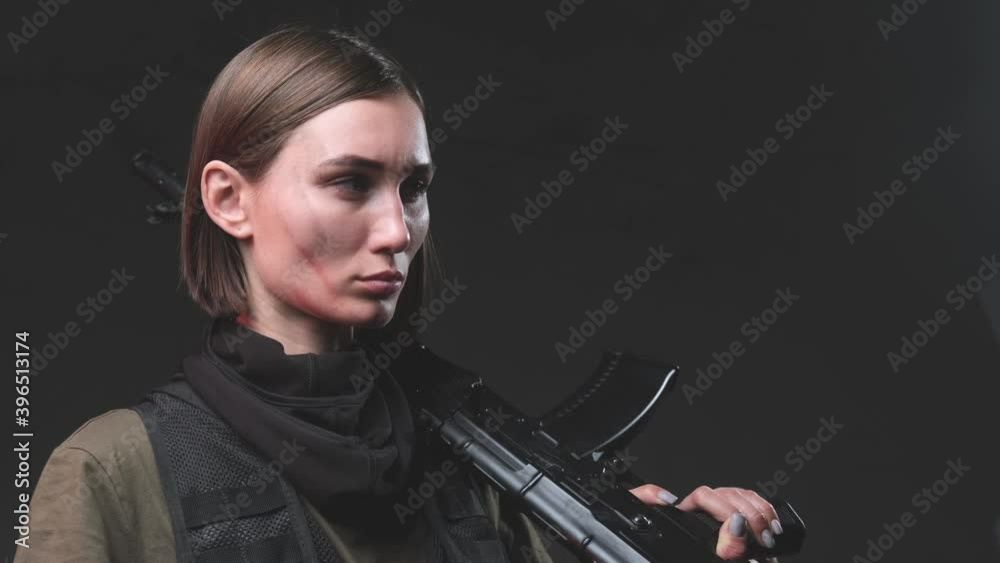 Stylish and serious woman with short haircut dressed in dark martial clothing poses in dark background rotating with ak 74 rifle on her shoulder. Stylish and serious woman with short haircut dressed in dark martial clothing poses in dark background rotating with ak 74 rifle on her shoulder.