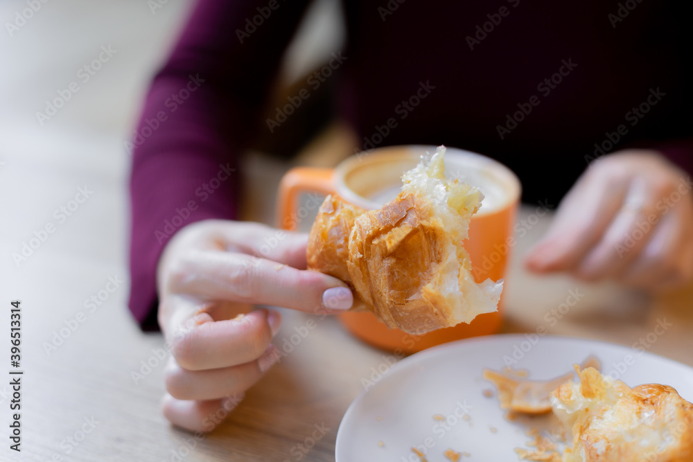 A girl has a croissant for Breakfast in a cafe