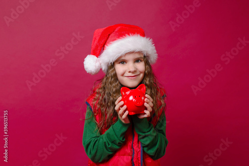 Cute girl kid holding a red piggy Bank or boar on a red background. Holidays  savings  traditions concept.