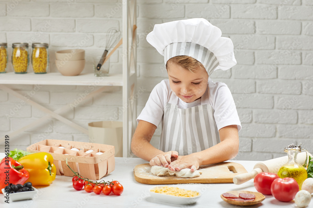 little child boy in chef hat and an apron knead the dough in the kitchen little child boy in chef hat and an apron knead the dough in the kitchen
