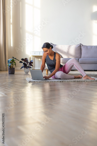 Smiling African-american woman preparing for a workout at home in front of a laptop monitor. Vertical photo.
