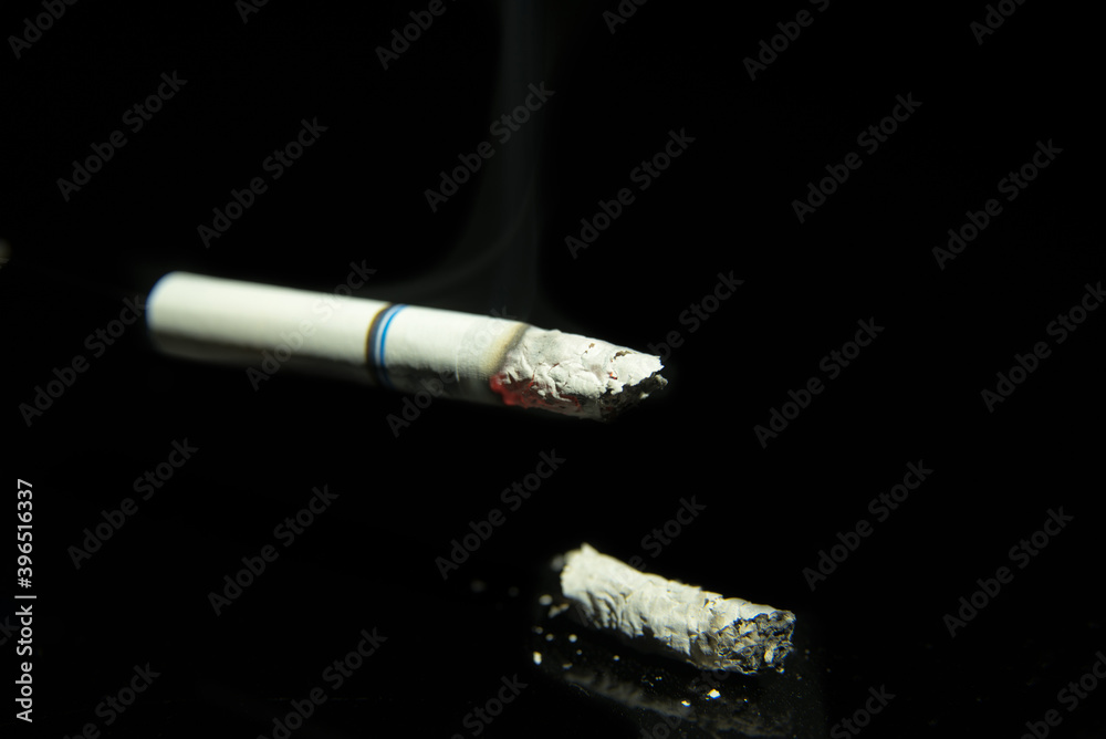 Obraz premium Lit cigarette with ash on a black background close-up, space for text, macro photography