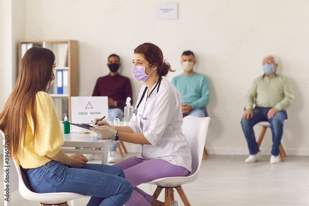 Doctor in face mask interviewing young woman before giving her antiviral vaccine Doctor in face mask interviewing young woman before giving her antiviral vaccine