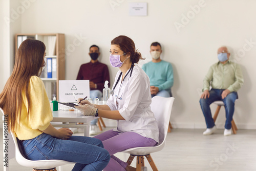 Doctor in face mask interviewing young woman before giving her antiviral vaccine