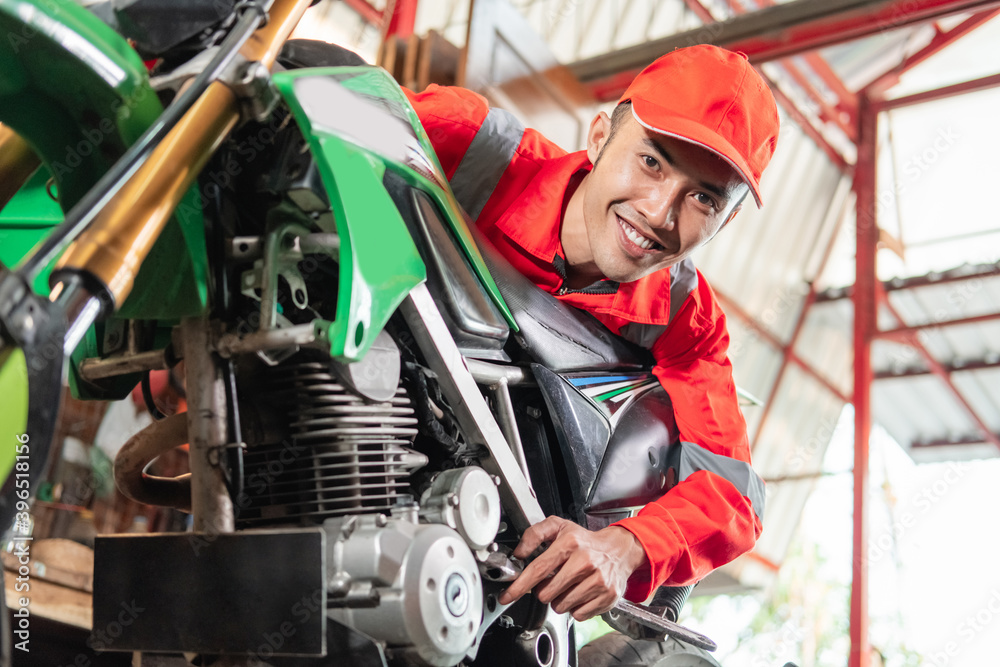 Smiling mechanic wearing wearpack and hat using a wrench to tighten the motorcycle bolt in the garage