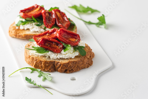 Bruschetta with sun dried tomatoes and arugula. Delicious breakfast or wine snack. White background, close-up view