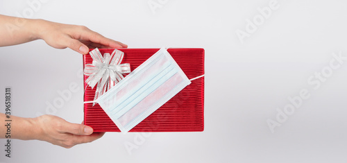 Hand is holding present or Gift box wrap with face mask and red color paper on white background. © nisara