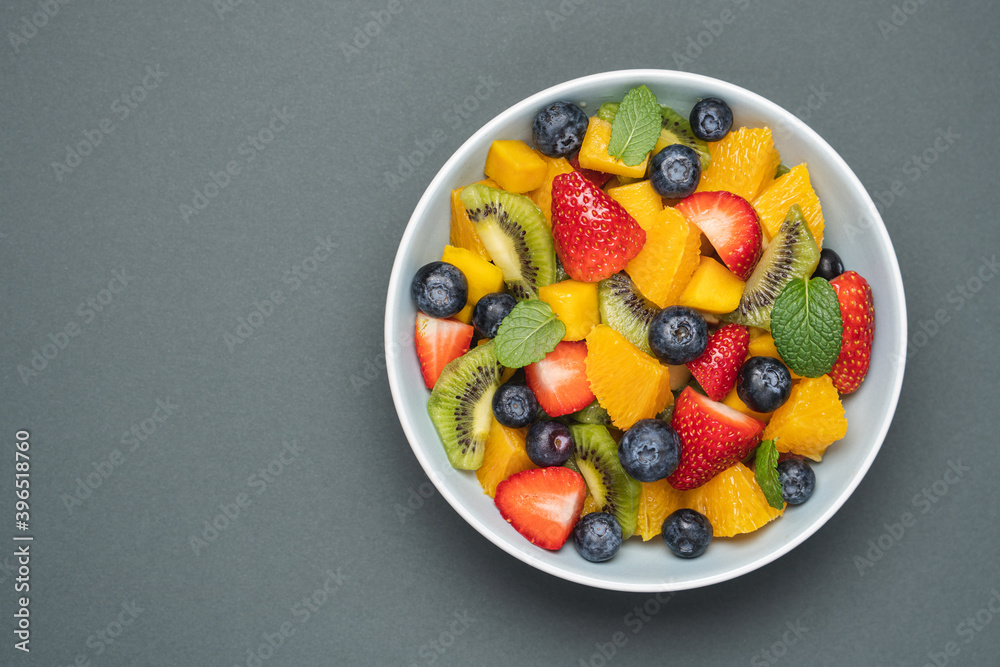 Fruit salad in bowl on grey background. Mango, kiwi, orange, apple, strawberry and blueberry berries