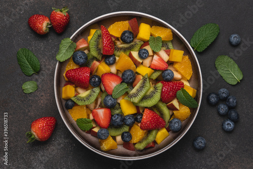 Fruit salad in bowl on brown background. Mango  kiwi  orange  apple  strawberry and blueberry berries