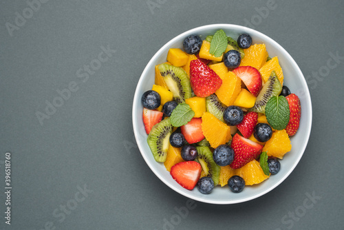 Fruit salad in bowl on grey background. Mango  kiwi  orange  apple  strawberry and blueberry berries