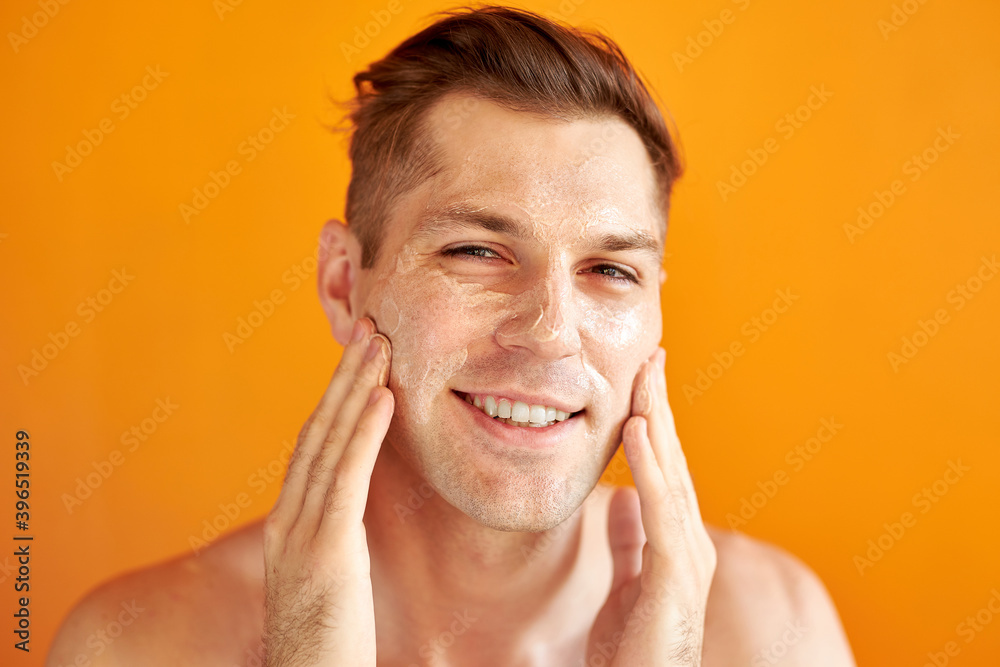 young caucasian man apply moisturizing face cream for healthy glowing skin, isolated over yellow background, handsome guy use nourishing facial balm, skincare, hygiene concept