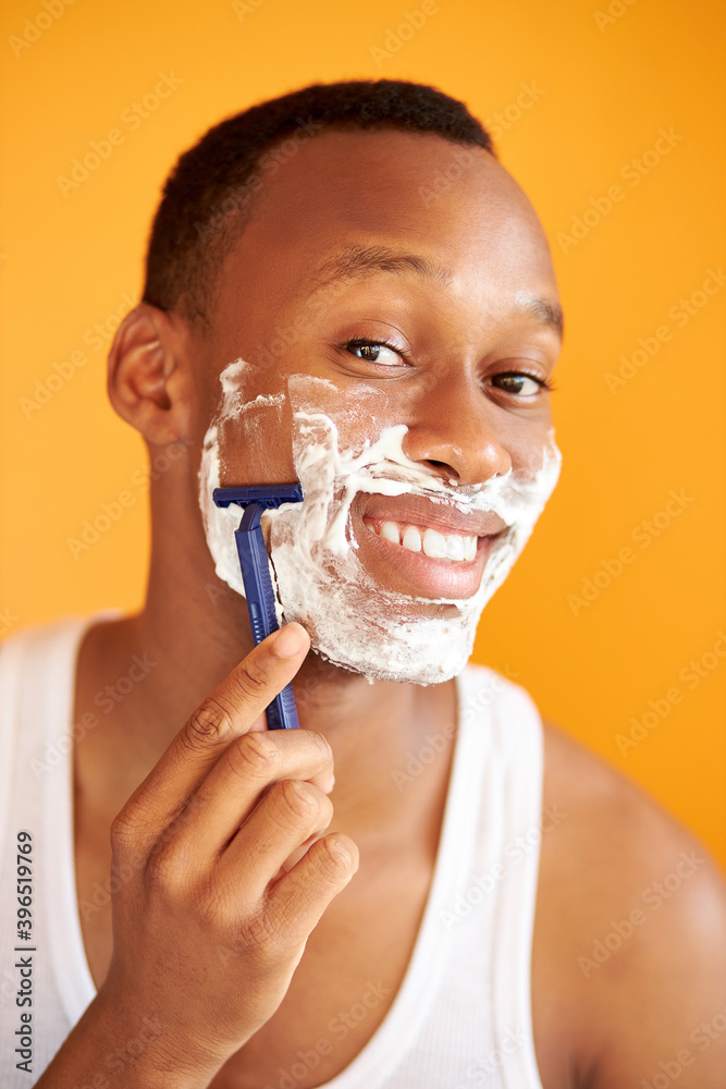 young black afro man shaving his face with the razor blade through shave foam, men skin care concept