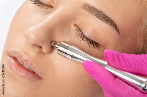 Beautiful girl with clean fresh skin.Cosmetologist makes  procedure microdermabrasion on the face against acne and blackheads on the nose. Women's cosmetology in the beauty salon. photo