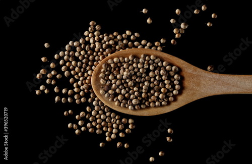 Coriander seeds with wooden spoon isolated on black background, top view