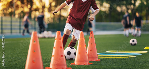 Football Player on Training Slalom Drill With Ball. Soccer Boy Running Between Red Training Cones on Grass Practice Field