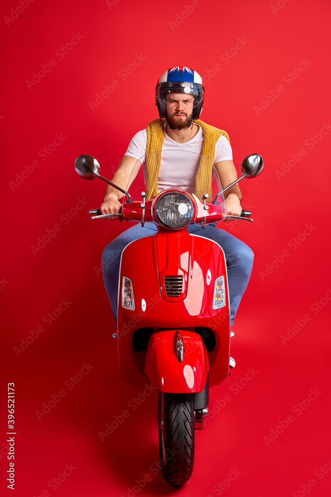 Fototapeta premium portrait of serious angry driver of motorcycle isolated over red studio background, young man in casual wear and helmet rushes