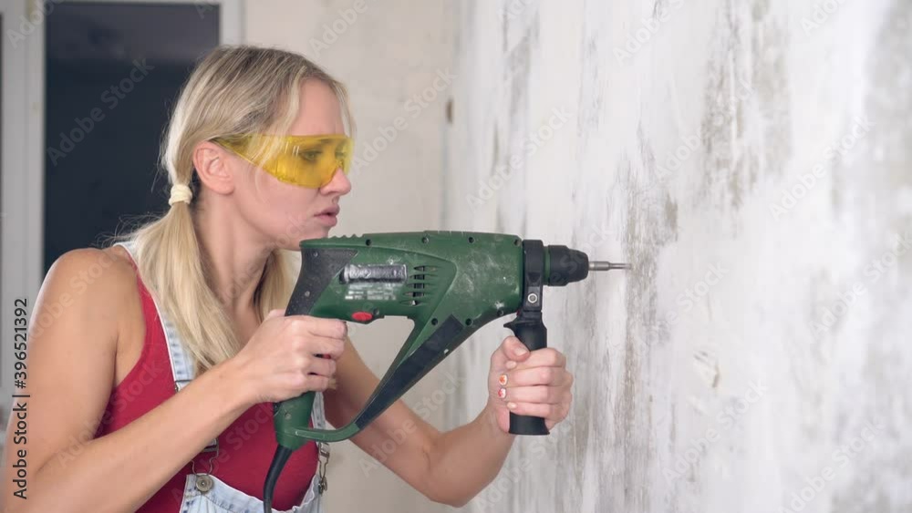 A young woman is drilling a wall with an electric hammer or drill