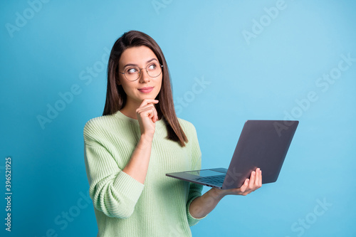 Minded clever girl hold laptop look empty space think decisions wear green pullover isolated on blue color background photo