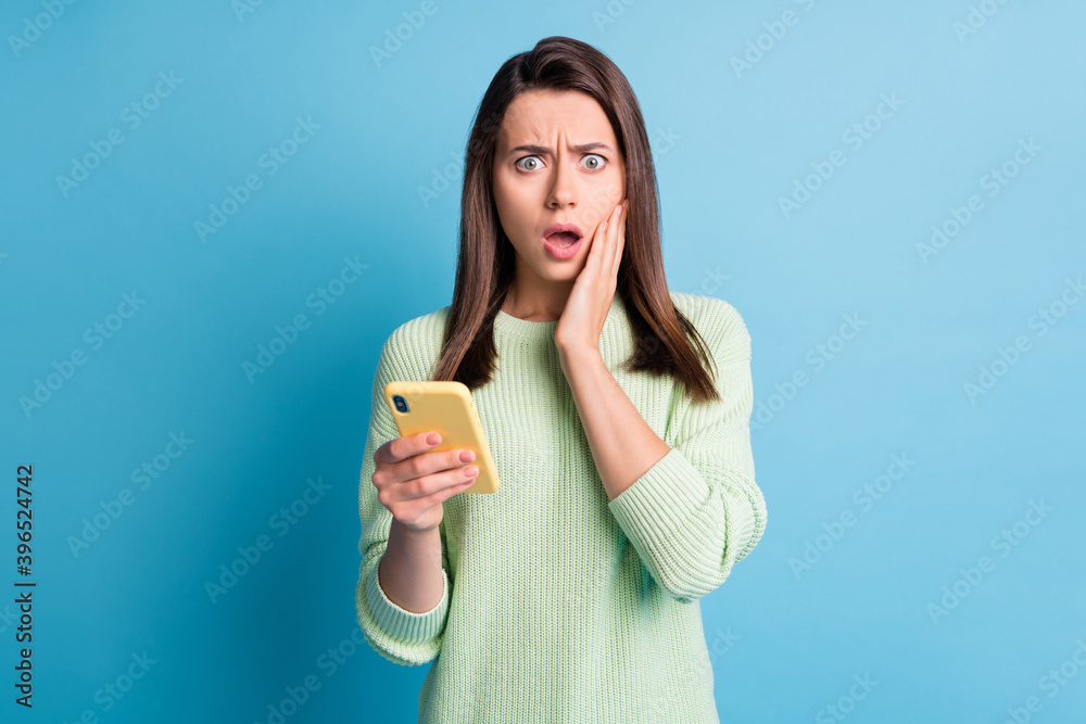 Photo portrait of worried woman touching face cheek with one hand holding yellow phone isolated on pastel blue colored background Photo portrait of worried woman touching face cheek with one hand holding yellow phone isolated on pastel blue colored background