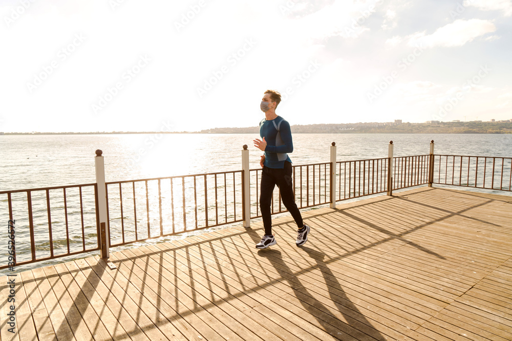healthy and handsome young male model running on the beach. The man wearing a mask is running by the sea in sportswear. Healthy man who does sports outside with his mask due to corona virus measures. healthy and handsome young male model running on the beach. The man wearing a mask is running by the sea in sportswear. Healthy man who does sports outside with his mask due to corona virus measures.