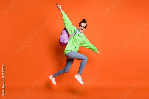 Full length photo portrait of schoolgirl making plane with hands jumping up isolated on vivid orange colored background