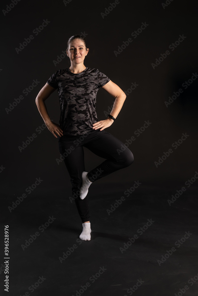 A fitness woman stands on an ode to her arm belt. Engaged in sports on a black background with a good look