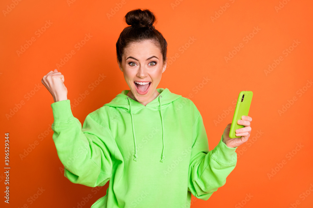 Photo portrait of woman celebrating with raised fist holding phone in one hand screaming isolated on vivid orange colored background Photo portrait of woman celebrating with raised fist holding phone in one hand screaming isolated on vivid orange colored background