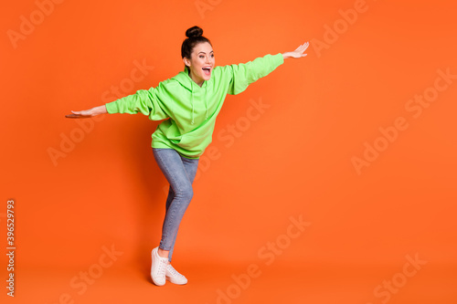 Photo portrait full body view of excited girl making plane with arms isolated on vivid orange colored background with blank space