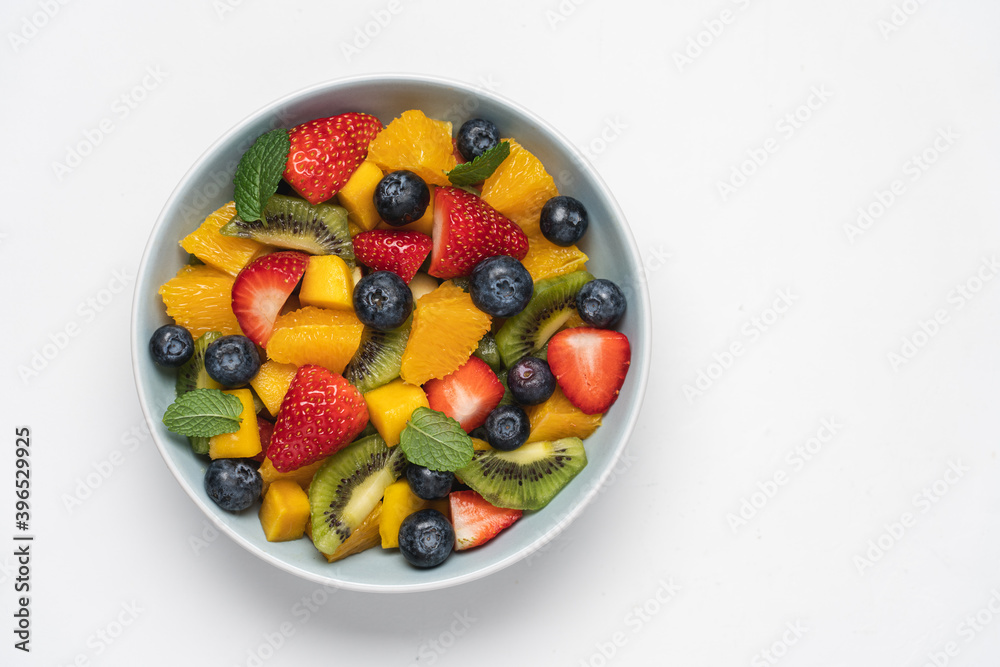 Fruit salad in bowl on white background. Mango, kiwi, orange, apple, strawberry and blueberry berries