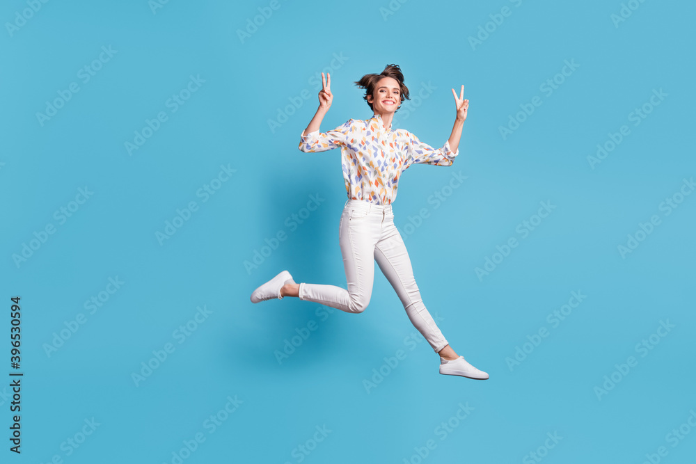 Full length photo of young girl happy positive smile jump show cool peace v-sign isolated over blue color background Full length photo of young girl happy positive smile jump show cool peace v-sign isolated over blue color background