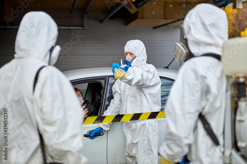 disinfectants checking documents and temperature at the entrance to the building, people in car, wearing protective suits, outdoors