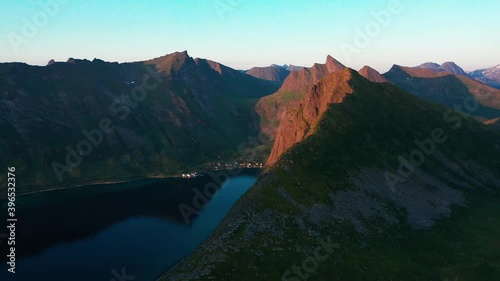 Aerial view around a sunlit mountain peak, overlooking the Steinfjord fjord, during midnight sun, in Senja, Norway - pan, drone shot photo