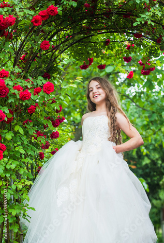 Feeling jubilant. happy childhood. beauty and fashion. pretty kid smell rose flower. spring and summer nature. little girl in garden. child enjoy blossom in park. small angel for bride. cute lady